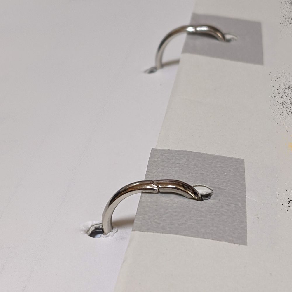 2穴パンチで穴を開けた書類をファイルにとじていて、穴から紙が破れてきたところを、マスキングテープで補強して再び穴を開けてとじた状態。マスキングテープが目立つ。