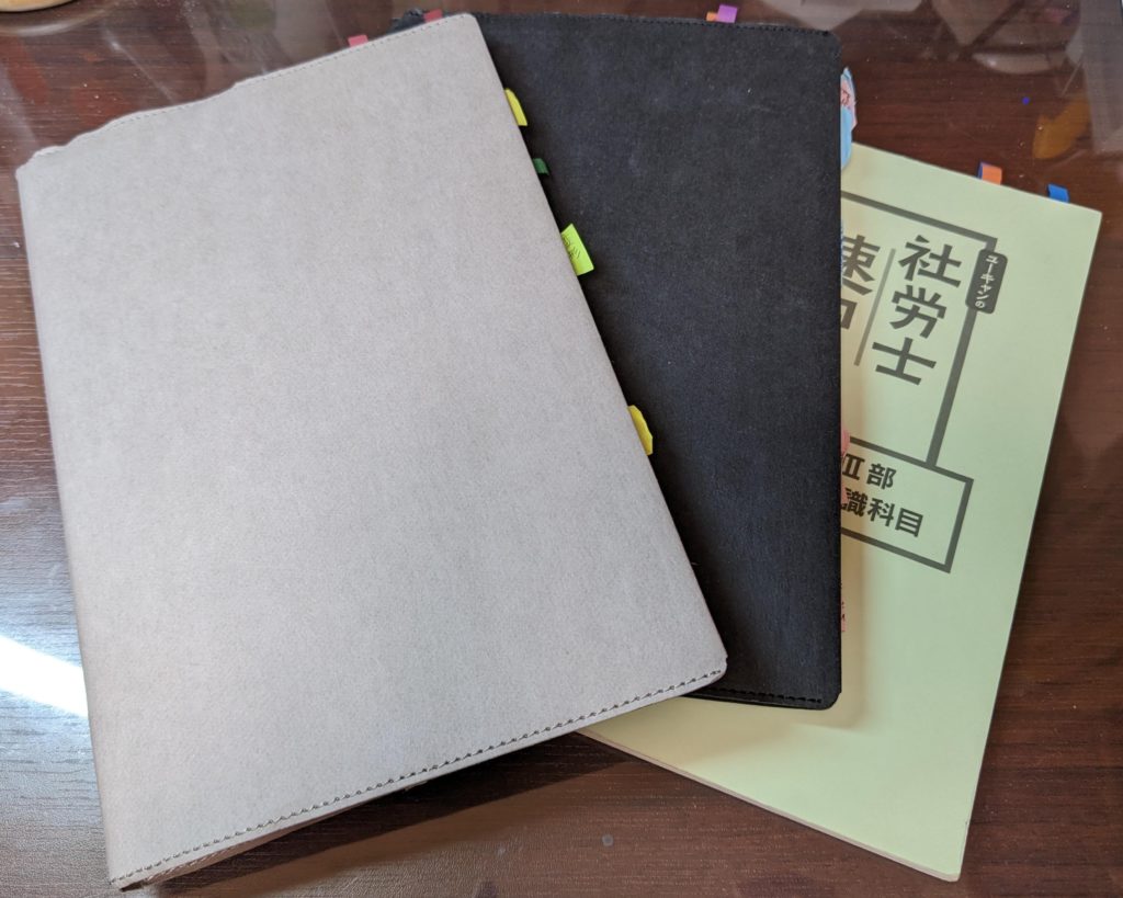 無印良品のグレーのノートカバーをつけたユーキャン社労士速習レッスンの労働のテキスト、ブラックのノートカバーをつけた社保のテキスト、カバーをつけていない一般常識のテキストの写真